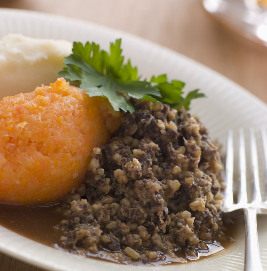 Une assiette de haggis accompagnée de purée de navet et de pommes de terre, garnie de persil, et une fourchette à côté du plat.