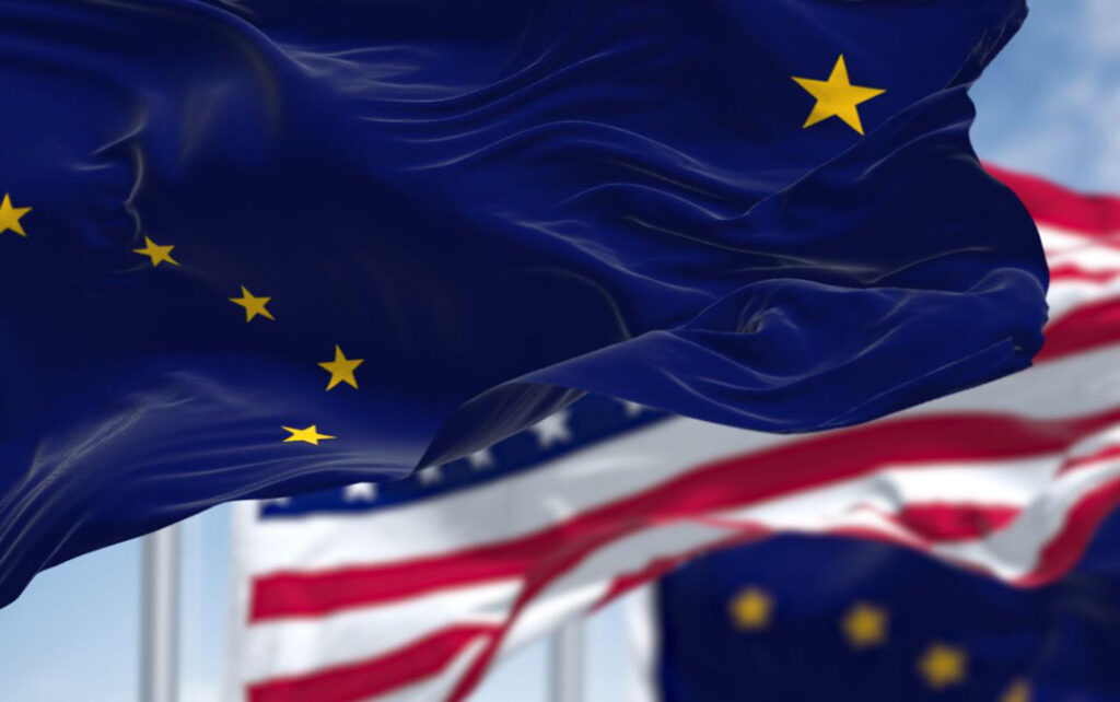 Drapeau de l'État de l'Alaska avec huit étoiles dorées au premier plan, recouvrant partiellement le drapeau américain à l'arrière-plan. Les deux flottent au vent.