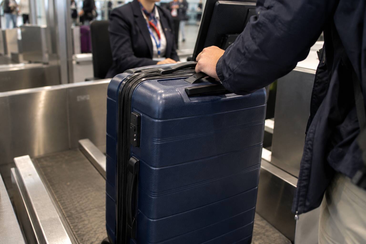 Une personne dépose une valise bleue sur le tapis roulant du comptoir d'enregistrement